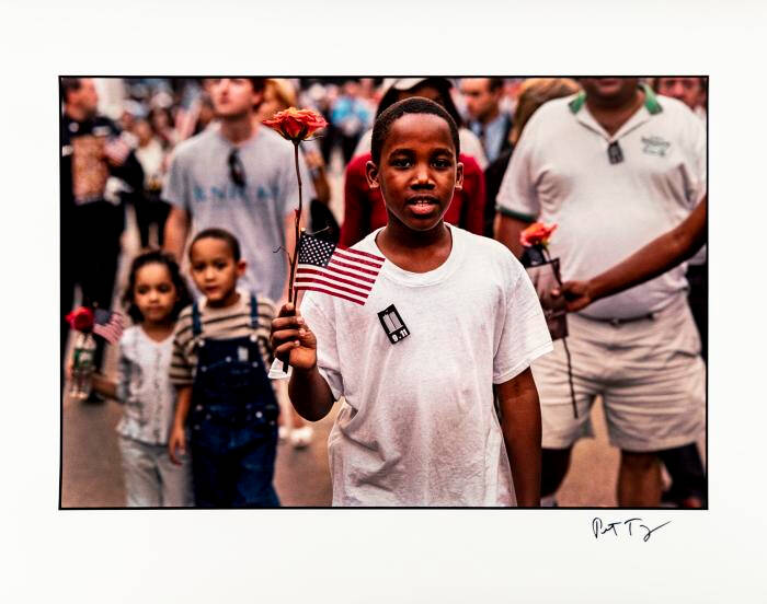 Photograph of a boy holding a small American flag in a crowd of people.